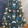 Božićno drvce sa zelenim iglicama, ukrašeno bijelim i srebrnim ukrasima, s bijelim tepihom