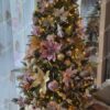 Umjetno božićno drvce sa zelenim granama, ukrašeno u glamur stilu, zlatno-ružičastim ukrasima i toplom bijelom rasvjetom