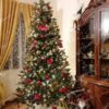Umjetno božićno drvce s tamnozelenim granama, ukrašeno zlatno-crvenim ukrasima, u dnevnoj sobi