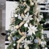 Umjetno božićno drvce sa zelenim granama, ukrašeno velikim bijelim i zlatnim ukrasima i vrpcama, u dnevnoj sobi