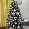 Umjetno božićno drvce s tamnim granama, ukrašeno bijelim ukrasima, s bijelim tepihom ispod drvca