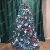 Umjetno božićno drvce s tamnozelenim granama, ukrašeno crvenim i zelenim ukrasima