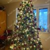 Visoko umjetno božićno drvce, tamnozelenih grana, gusto ukrašeno ukrasima u boji i toplom rasvjetom