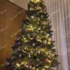 Visoko umjetno božićno drvce s tamnozelenim granama, ukrašeno ljubičastim i srebrnim ukrasima