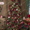Visoko i gusto umjetno božićno drvce, blijedozelenih grana, obilno okićeno crvenim ukrasima