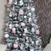 Visoko umjetno božićno drvce sa snježnim granama, ukrašeno ružičastim i bijelim ukrasima