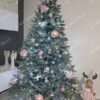 Umjetno božićno drvce s ledenozelenim granama, ukrašeno srebrno-ružičastim ukrasima.
