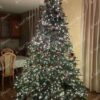 Visoko i široko umjetno božićno drvce, gusto okićeno crvenim i zlatnim ukrasima i toplom bijelom rasvjetom
