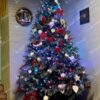 Visoko i široko umjetno božićno drvce s bijelim vrhovima grana, ukrašeno bijelim i crvenim božićnim ukrasima u kutu dnevne sobe.