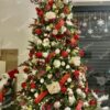 Umjetno božićno drvce sa zelenim granama, gusto okićeno crveno-bijelim božićnim ukrasima, pristaje uz bijeli tepih i Djeda Božićnjaka