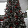 Snijegom prekriveno umjetno božićno drvce s crveno-bijelim božićnim ukrasima