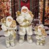 Vianočná dekorácia Santa Claus Bielo-zlatý, oblečený ma biely kabát s zlatou dekoráciou a v ruke drží macka